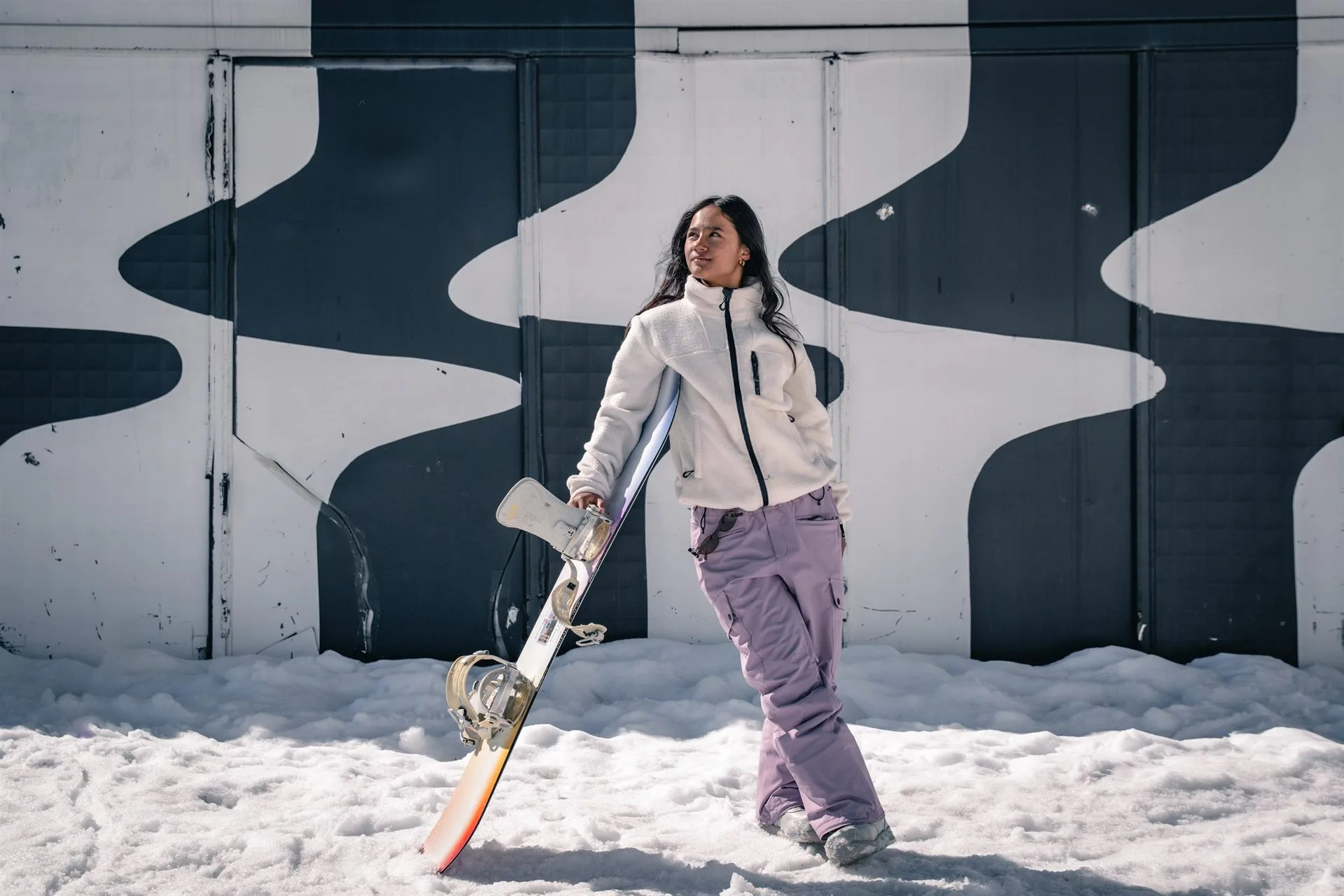 Zazi Betari, Indonesian Snowboard Girl, holding her board against a graphic mural